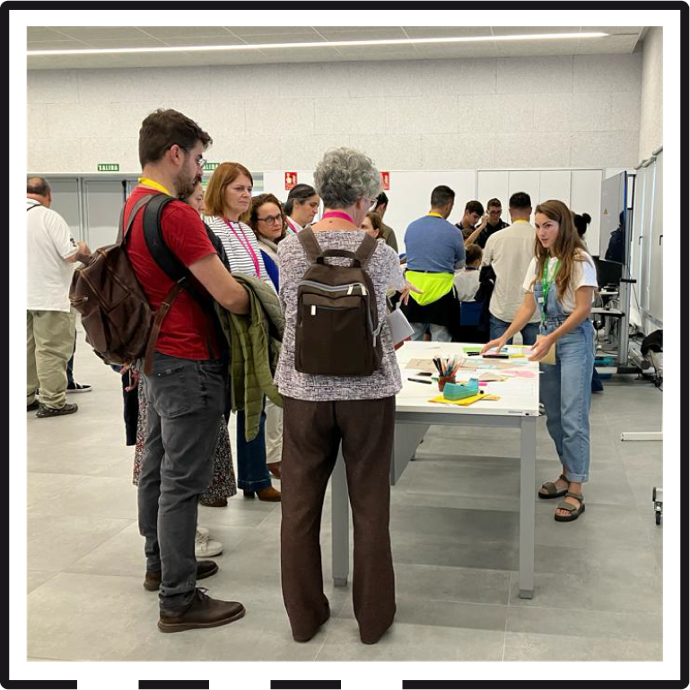 En una amplia sala llena de participantes distribuídos en diferentes mesas, Ornella dirige un taller colaborativo