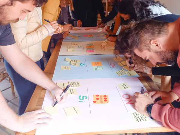 Varias personas están concentradas participando concentradas en un taller, trabajando en una cartulina conjunta